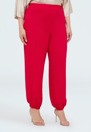 Straight red pants with elastic cuffs worn with beige high-heeled sandals and a beige satin top, shown from waist to feet.