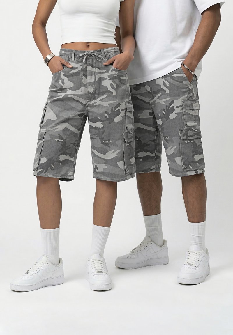 Δύο άτομα που φορούν γκρι καμουφλάζ cargo σορτς, λευκά αθλητικά παπούτσια και λευκά τοπ, στέκονται με τα χέρια στις τσέπες σε απλό φόντο.