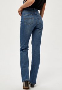 Modré džínové kalhoty s vysokým pasem, rozšířenými nohavicemi a dvěma zadními kapsami. Tkanina vykazuje mírné vyblednutí a lemy jsou prošívané.