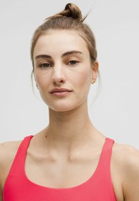 Modelo femenina vestida con una blusa sin mangas de color rosa brillante, con un escote redondeado y una textura suave, y el cabello recogido en un moño.