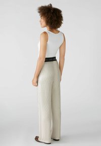 Witte geribde tanktop gecombineerd met wijde, glanzende zilveren tekstuurbroek met een zwarte elastische tailleband.