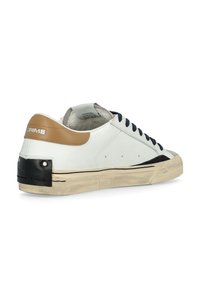 Sneaker in pelle bianca con lacci blu navy, un tassello sul tallone color nocciola e un accento nero sul tallone. Presenta una suola in gomma consumata e cuciture decorative.