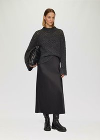 Grijze, gebreide trui met grote gaten, gecombineerd met een zwarte satijnen maxi-rok. Zwarte leren schoudertas en zwarte laarzen tot de knie.