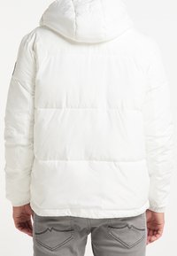 Weißer Pufferjacke mit Kapuze, ausgestattet mit einem gesteppten Design und elastischen Bündchen. Die Rückansicht zeigt minimale Markenkennzeichnung und eine glatte Textur.