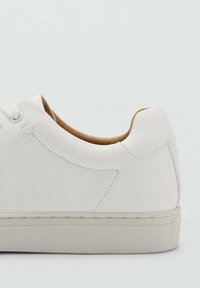 Zapatilla blanca con parte superior de cuero liso, puntera redondeada, diseño minimalista, costuras ligeras y suela de goma color crema.