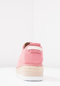 Chaussure espadrille en daim rose avec semelle intermédiaire en jute tissé et semelle extérieure en caoutchouc blanc, présentée de l'arrière sur un fond blanc.