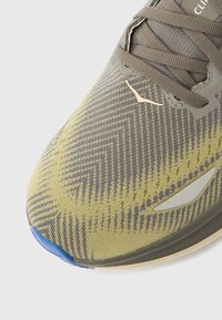 Ελαφρύ αθλητικό παπούτσι με υφή και επάνω μέρος σε κίτρινο-πράσινο και γκρι μοτίβο. Διαθέτει γκρι λογότυ πα και μπλε λαστιχένιο κάλυμμα στα δάχτυλα.