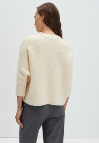 Strickpullover in Cremefarben mit strukturiertem Muster, Oversize-Passform und 3/4-langen Ärmeln, kombiniert mit grauer Hose.