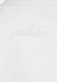 Gros plan sur un tissu blanc côtelé avec un texte manuscrit blanc brodé subtilement "smildose" à la surface.