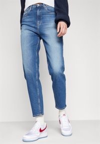 Jeans rectos de color azul claro con textura desvaída y cinco bolsillos. Combinados con zapatillas blancas con acentos rojos y calcetines blancos.