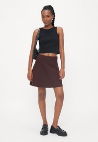 Svart crop-top, burgunder vid skjørt og svarte klumpete loafers. Antrekket har et enkelt design med en glatt tekstur og en strukturert passform.