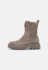 Bottine en suède taupe avec fermeture éclair à l'avant, bout rond, tirette et semelle épaisse crantée sur un fond blanc.