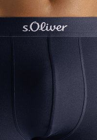 Muške bokserice tamnoplave boje, glatke teksture, s mekim, elastičnim pojasom s vezom "s.Oliver" u bijeloj boji.