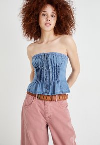 Top de ganga sem alças com textura franzida, frente com botões e detalhe de laço. Combinado com calças largas rosa claro e um cinto castanho.