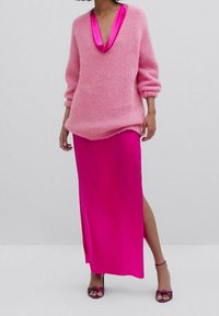 Różowy sweter dzianinowy z dekoltem w serek i luźnym krojem, w połączeniu z jasnoróżową satynową spódnicą do kolan z bocznym rozcięciem i dopasowanymi szpilkami.