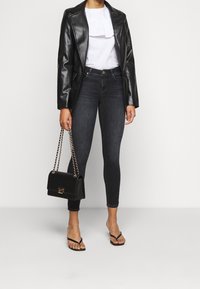 Blazer de cuero negro, blusa blanca con volantes, vaqueros ajustados oscuros, bolso negro con cadena y chanclas negras. Look sencillo y ajustado.