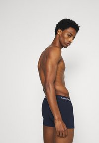 Boxer-briefs bleu marine avec une texture douce et une taille élastique mettant en avant le logo « LACOSTE » affiché en blanc.