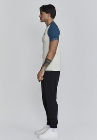 Fitted crèmewit t-shirt met blauwe korte mouwen met een logo, gecombineerd met zwarte taps toelopende joggers en witte sneakers.