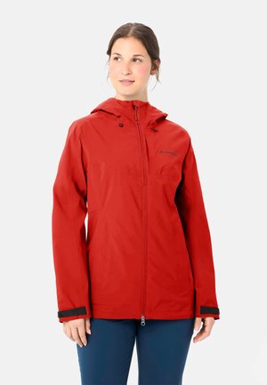 Donna che indossa una giacca impermeabile rossa con cappuccio, zip frontale e polsini regolabili, in piedi davanti a uno sfondo chiaro uniforme.