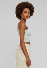 Mint green, cropped ribbed tank top with thin straps, paired with beige high-waisted pants featuring a side pocket and a slit hem detail.
