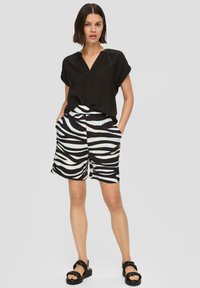 Czarny top z dekoltem w serek, zestawiony z krótkimi spodniami w paski zebry w białym i czarnym kolorze, z elastycznym pasem i bocznymi kieszeniami. Na nogach czarne sandały.