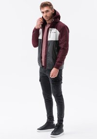 Mörkröd och grå vindjacka med en vit panel, dragkedja framtill och huva, i kombination med svarta slim fit-jeans och svarta sneakers.