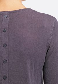Lila, stickad kofta med rund halsringning, texturerad tyg och sex små, runda svarta knappar längs ryggen.