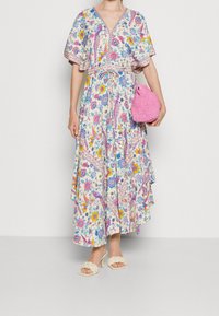 Florales Maxikleid mit V-Ausschnitt, Flatterärmeln und Gürtel. Es hat mehrfarbige Blumen- und Paisleymuster. Kombiniert mit einer pinkfarbenen, gewebten Handtasche.