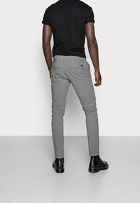 Šedé strečové kalhoty se slim fit střihem, s jemnou texturou a dvěma zadními kapsami. Kombinované s černou košilí s krátkým rukávem a černými kotníkovými botami.