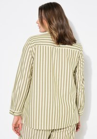 Camisa de manga larga a rayas en verde oliva claro y crema con puños abotonados y detalle en el yugo trasero, hecha de una tela suave y transpirable.