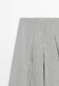 Pantalon large à rayures verticales noires et blanches avec des plis, présenté de la taille au milieu de la cuisse sur fond blanc.