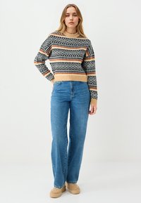 Gebreide trui met geometrische zwart-wit patronen en roest-oranje strepen, ronde halslijn, gecombineerd met hoge taille blauwe jeans en tan schoenen.