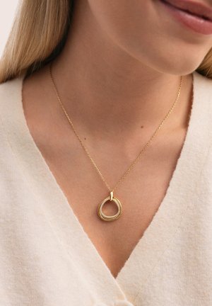 Collar de oro con un colgante circular entrelazado que tiene un borde texturizado y piedras de imitación incrustadas, colgado de una cadena delicada.