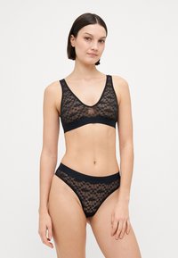 Juodas nėrinių bralette'as ir atitinkamos kelnaitės, pasižyminčios gėlėmis, permatomu audiniu ir elastinga juosta su prekės ženklo logotipu.