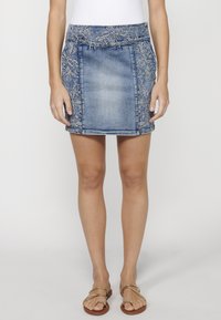 Jupe mini en denim avec des broderies florales délicates au niveau de la taille et sur les côtés, présentant une coupe ajustée et un délavage bleu clair à moyen.