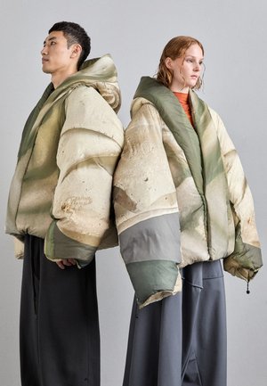 Donsjacks in tan en groene tinten, met een textuurstof en een capuchon, in een oversized pasvorm. Gecombineerd met donkere, losse broeken.