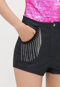 Shorts noirs avec poches, présentant un design à franges en perles métalliques. Tissu lisse avec une coupe ajustée et un détail de ceinture cloutée.