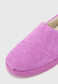 Violetiniu zomšiniu slip-on tipo batu su apvaliu pirštu, dekoratyvine siūle ir tekstūruotu toniniu guminio pado. 