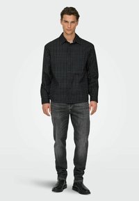 Tamsi languota marškiniai su atverčiamu apykakliu, juodos ir mėlynos spalvų languota spalva, derinami su pilkomis džinsine kelnėmis ir juodais odiniais batais.