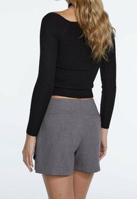 Schwarz geripptes Langarmoberteil kombiniert mit grauen Shorts mit tailliertem Schnitt und Gesäßtaschen, von einer leicht schrägen Rückansicht präsentiert.