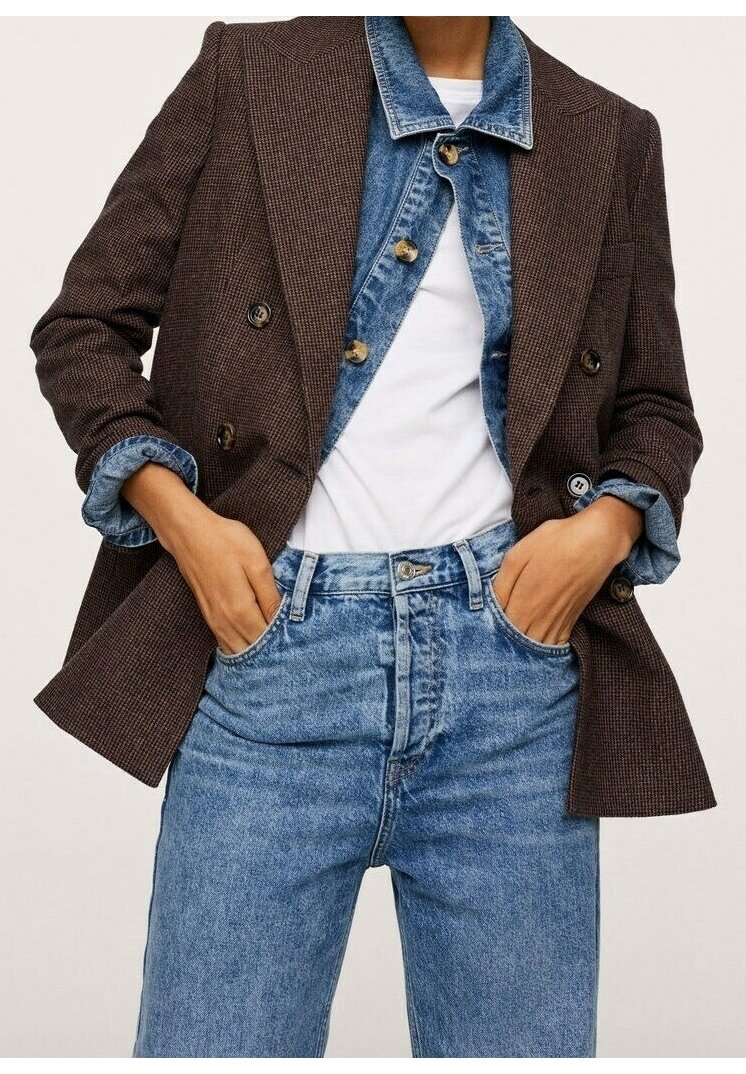 Bruine houndstooth dubbelbreasted blazer gedragen over een blauwe denim jas, gecombineerd met lichtgekleurde denim jeans met hoge taille. Knopen zichtbaar.