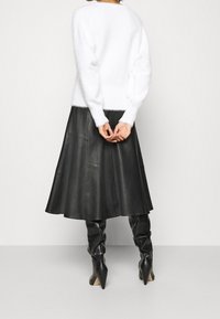 Plüschiger weißer Pullover mit langen Ärmeln, kombiniert mit einem schwarzen Leder-A-Linien-Rock und hohen schwarzen Stiefeln mit Absatz. Glatte Textur und markante Nähte.