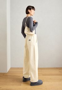 Cremefarvede vide bukser med sidelommer, tekstureret grå langærmet top og en lille beige håndtaske. Grå pelsforede støvler fuldender looket.