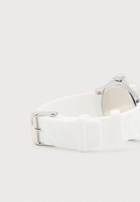 Bracelet de montre en silicone blanc avec boucle en métal, partiellement connecté à un boîtier de montre argenté, sur un fond blanc.