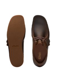 Bruna läderskor med rund form, mockasin-design och kontrastsöm. Slät textur med gummisula. Clarks-logotyp synlig.
