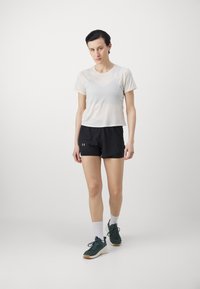 Sporty antrekk med en lett, pustende hvit t-skjorte med korte ermer og svarte treningsshorts. Kombinert med grønne joggesko og hvite sokker.