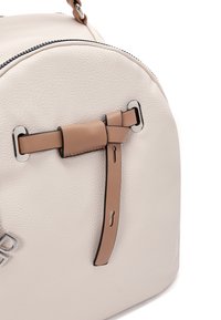 Crème leren tas met een gestructureerd oppervlak, voorzien van een bruine banddetail en zilveren hardware accenten, ronde vorm en ritsluiting.