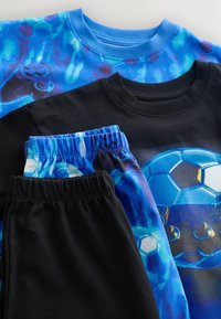 Deux ensembles de vêtements pour enfants avec un schéma de couleurs bleu et noir ; un t-shirt affiche un graphisme de ballon de football bleu et de manette de jeu.