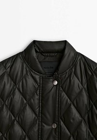 Veste noire matelassée avec des surpiqûres en forme de losange, col montant et deux boutons-pression argentés visibles sur la patte de boutonnage avant.