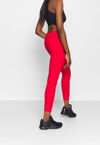 Rode leggings met een strakke pasvorm en enkelmanchetten, gemaakt van elastisch materiaal, gecombineerd met zwarte sportieve schoenen en een zwarte crop top.